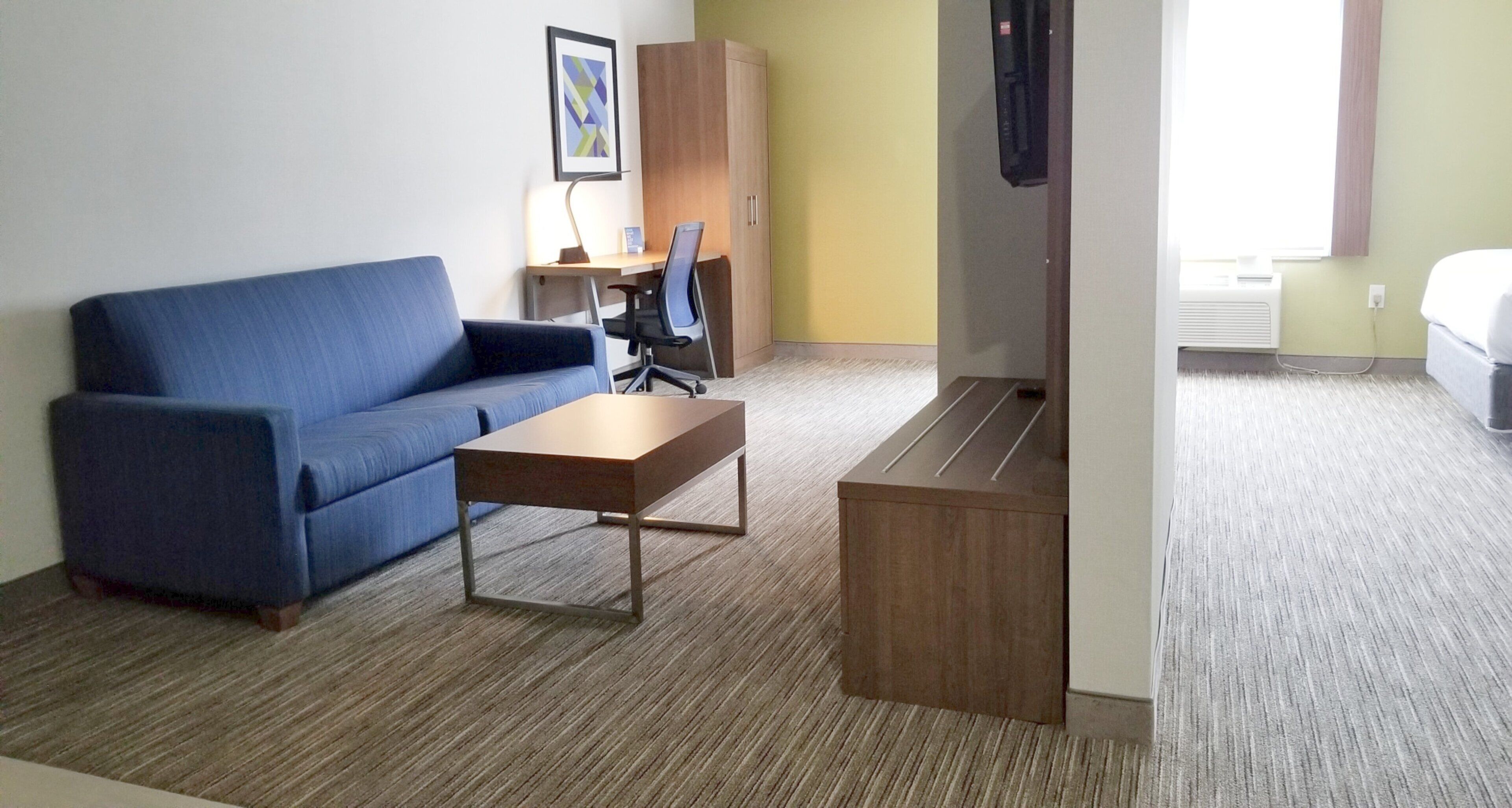 Een hotelkamer met een blauwe bank, een houten salontafel, een bureau met stoel, een kledingkast en een bed.