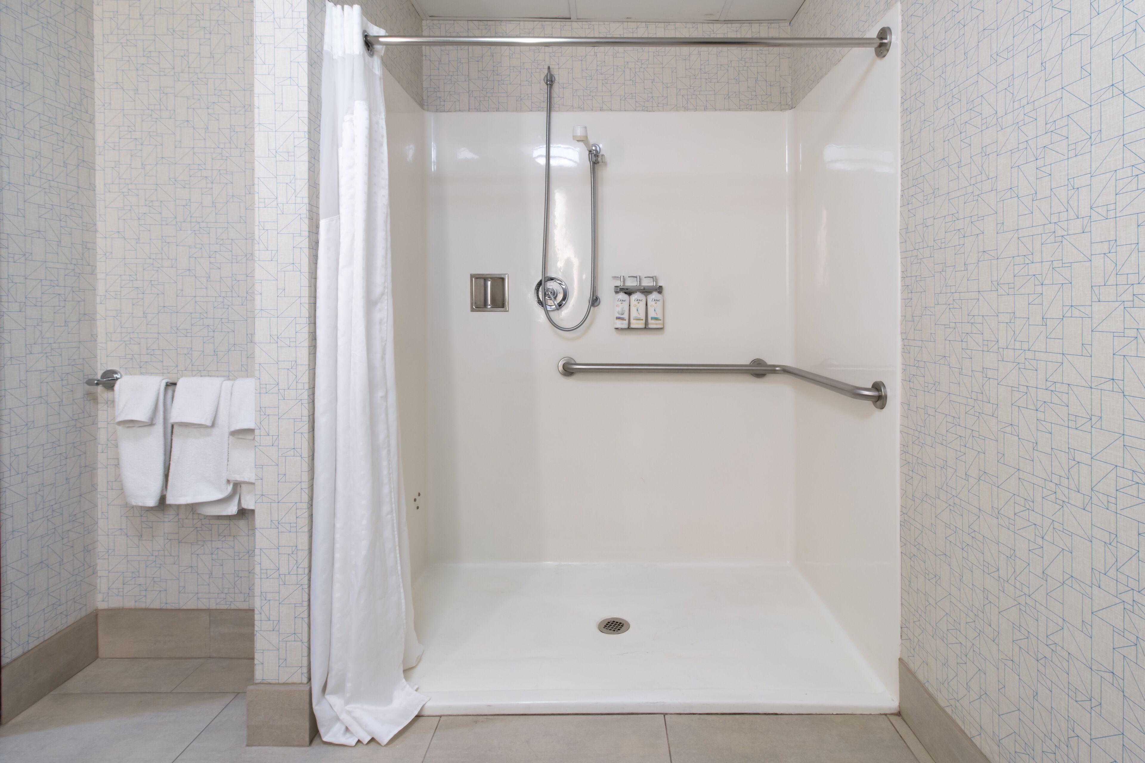 Une douche à l’italienne équipée d’une barre d’appui, d’un pommeau de douche et d’un panneau de commande.