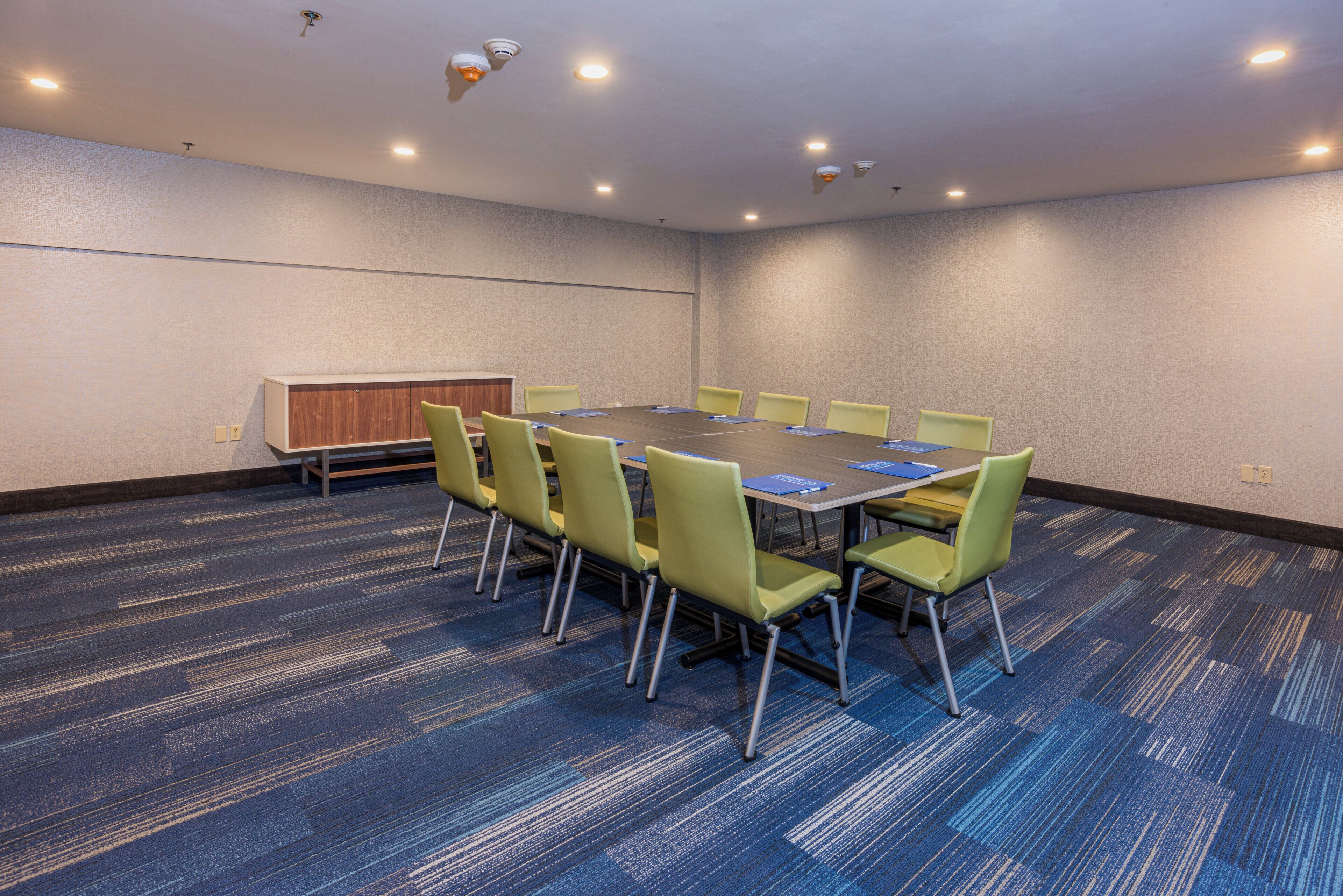 A conference room with a round table, chairs, a cabinet, and carpeted flooring.