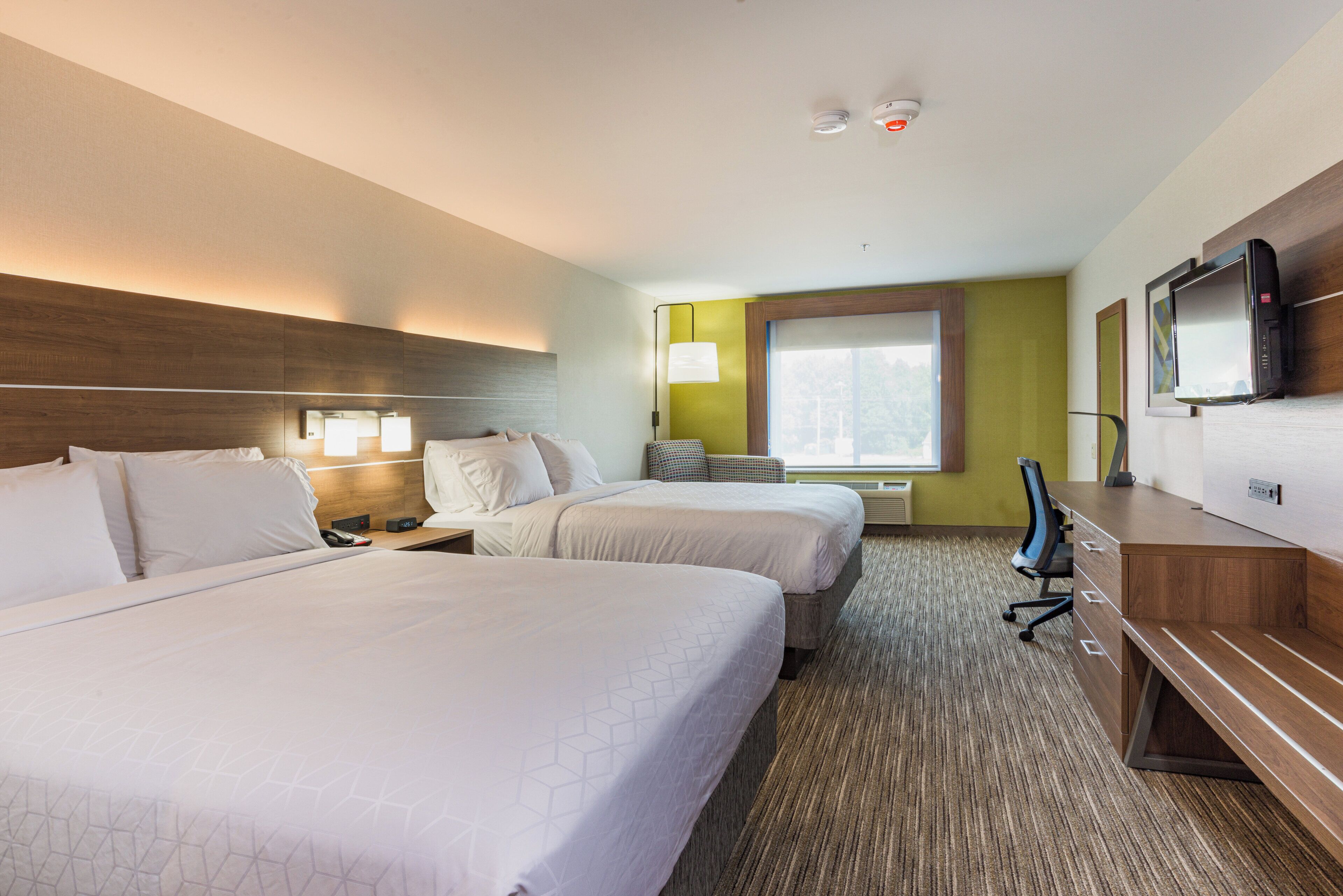 A hotel room with two beds, a desk, a chair, a television, and a window with a view.