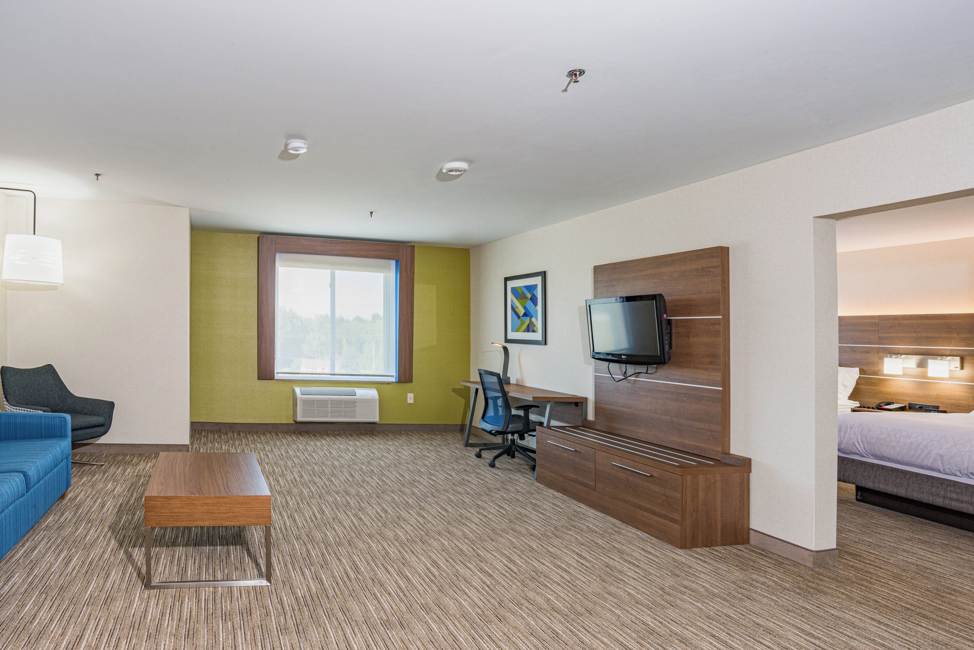 A hotel room with a bed, a desk, a chair, a television, and a window.