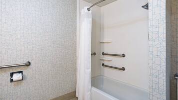 Baño con ducha, barras de apoyo y portarrollo para papel higiénico.
