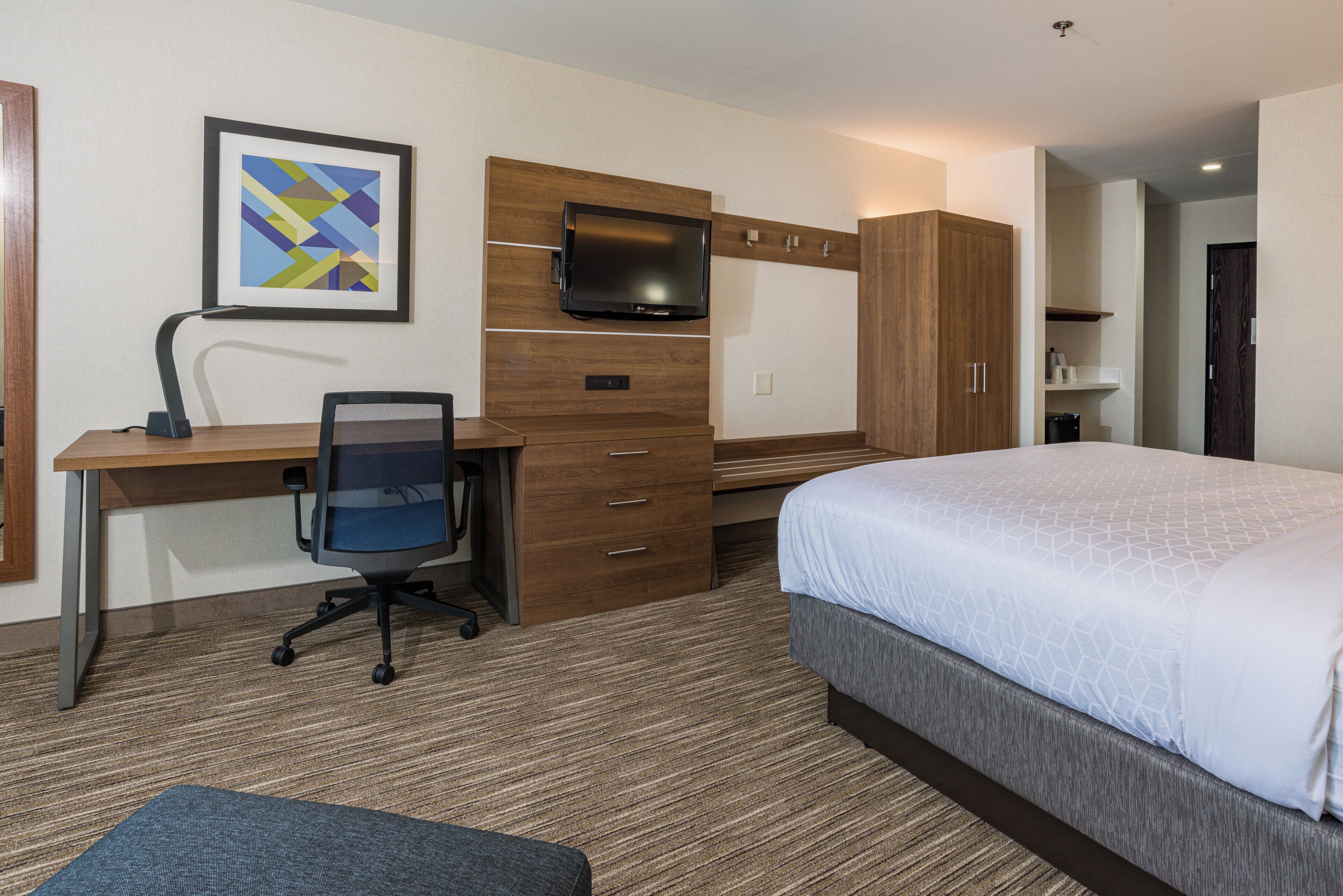 Une chambre d’hôtel comprenant un lit, un bureau avec une chaise, une télévision et une armoire.