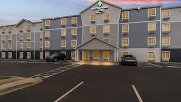 A multi-story hotel with a central entrance, parking spaces, and a clear sky.