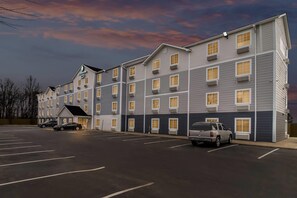 A multi-story hotel with a parking lot, several cars parked, and a clear sky. - WoodSpring Suites Memphis East I-40 (Memphis)