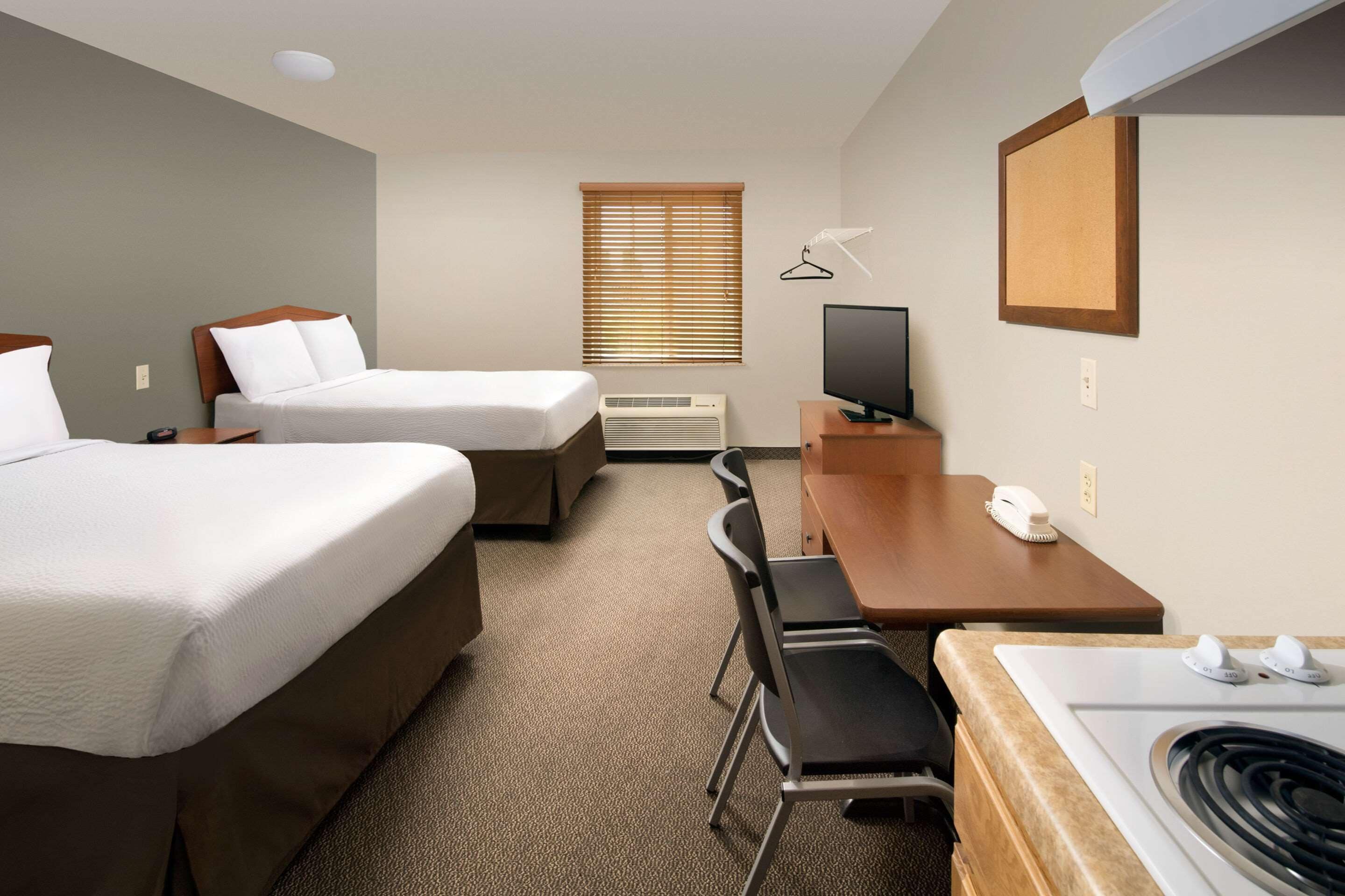 A hotel room with two beds, a desk, a chair, a television, a heater, and a window with blinds.
