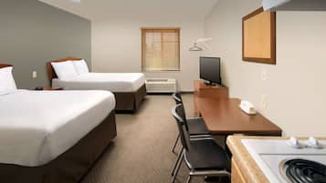A hotel room with two beds, a desk, a chair, a television, a heater, and a window with blinds.