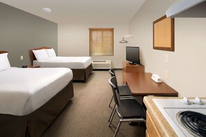 A hotel room with two beds, a desk, a chair, a television, a heater, and a window with blinds. - WoodSpring Suites Memphis East I-40 (Memphis)