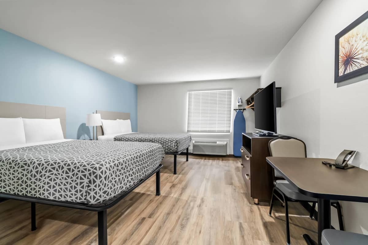 A hotel room with two beds, a desk, a chair, a television, and a window with blinds.