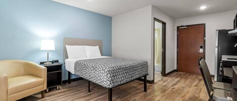 A hotel room with a bed, a chair, a desk, a lamp, and a door.