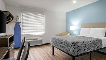 A hotel room with a bed, desk, chair, and a window with blinds.