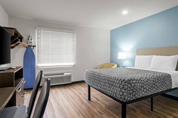 A hotel room with a bed, desk, chair, and a window with blinds. - WoodSpring Suites Memphis East I-40 (Memphis)