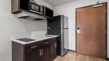A compact kitchen with a microwave, refrigerator, sink, and wooden door.