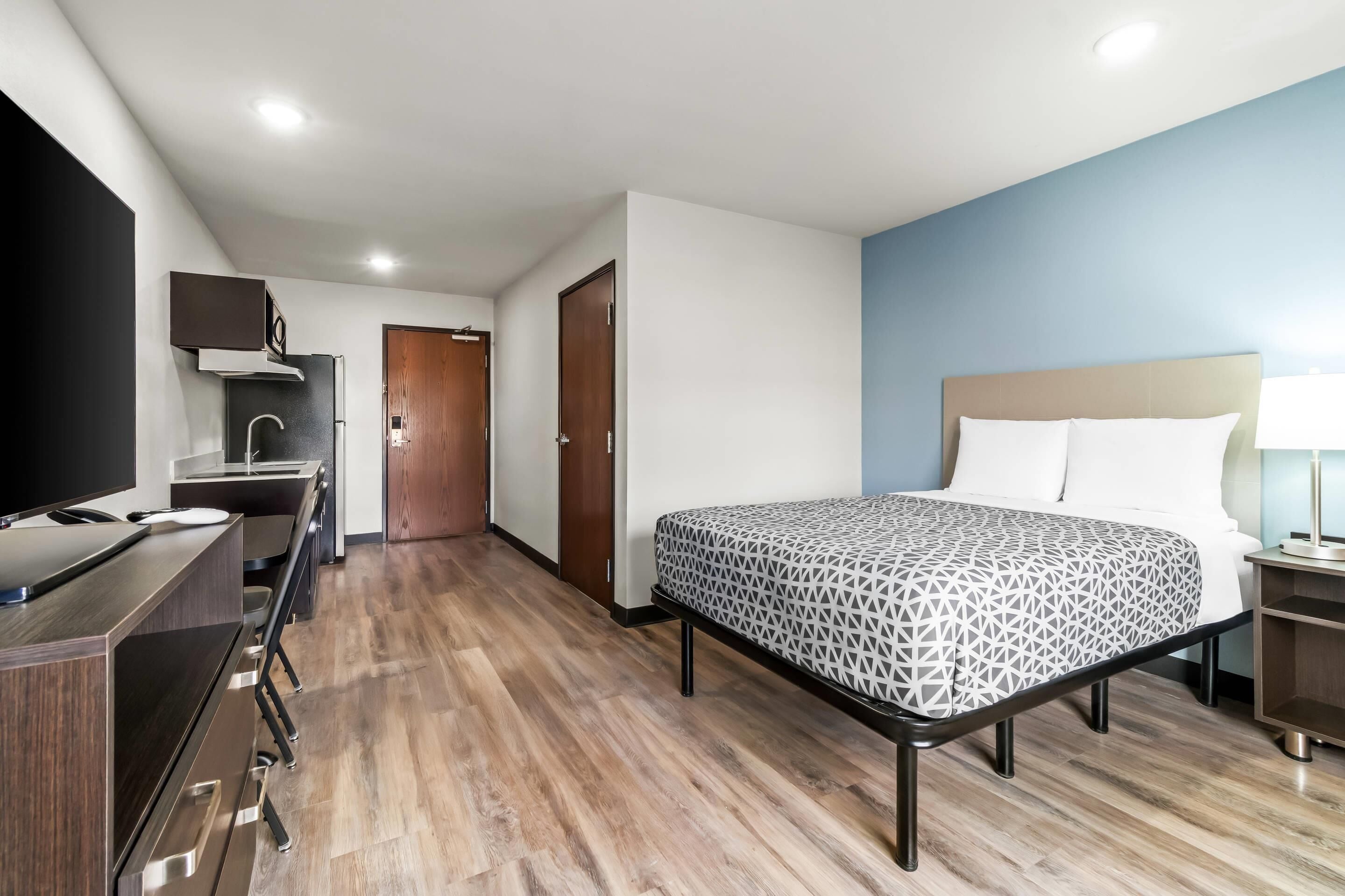 Una camera d'albergo con un letto, una scrivania, una televisione, un armadio e un bagno.