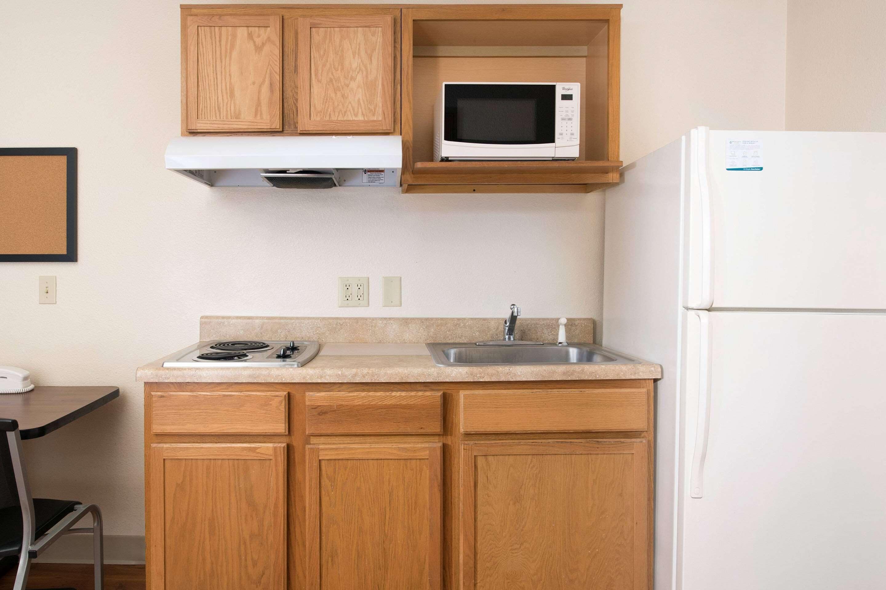 A compact kitchen with wooden cabinets, a microwave, a sink, and a refrigerator.
