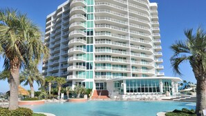 Un hotel de varios pisos con piscina, palmeras y un cielo azul despejado.