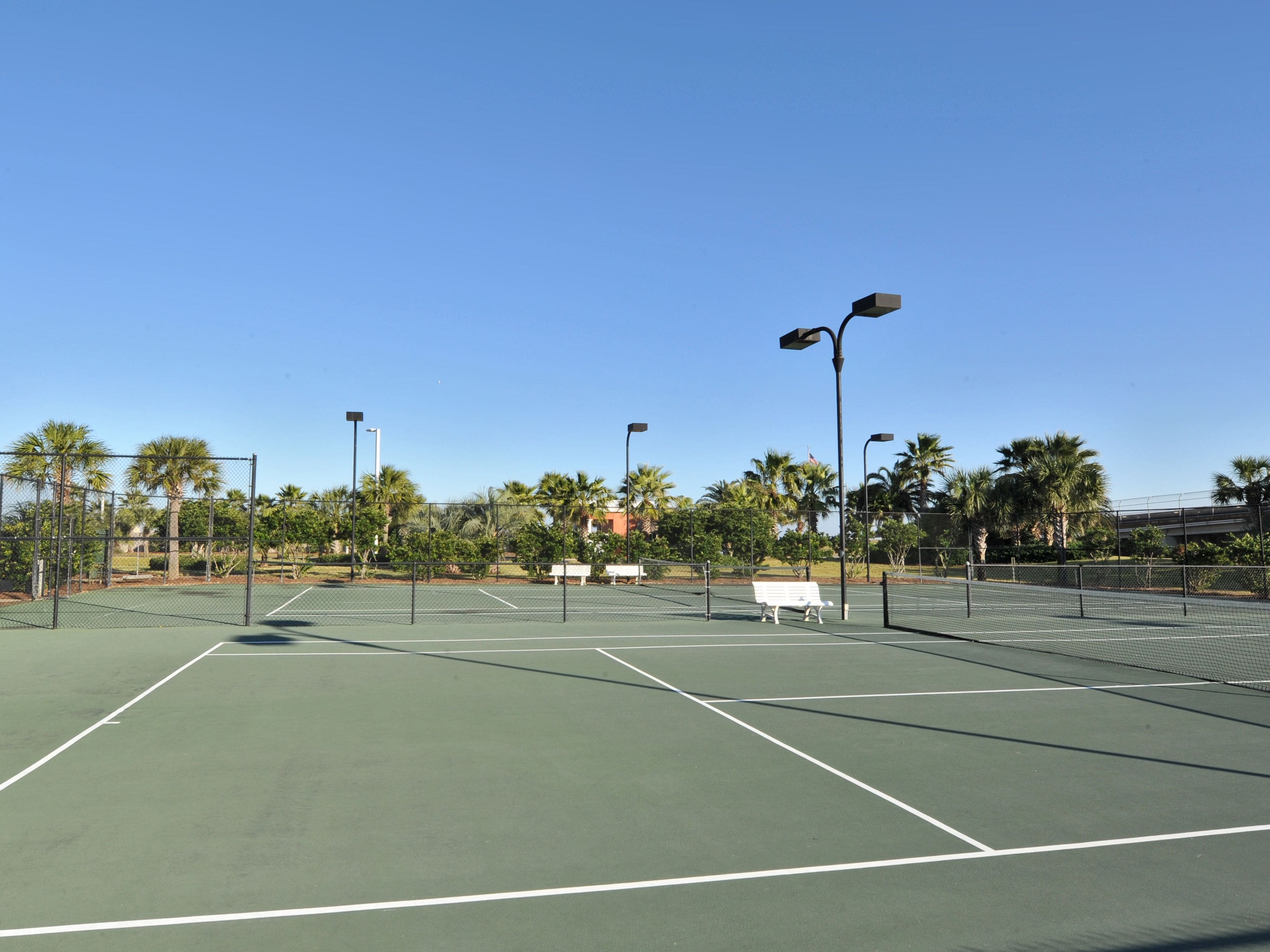 Ein Tennisplatz mit Zaun, Bänken und Straßenlaternen.