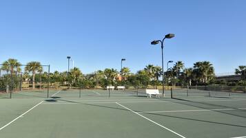 Ein Tennisplatz mit Zaun, Bänken und Straßenlaternen.