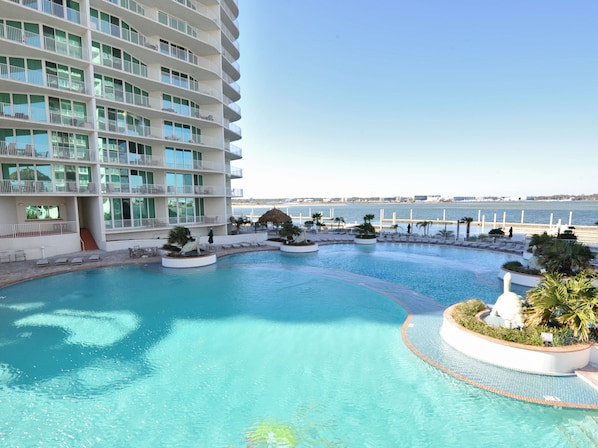 A resort pool area with a large building, multiple balconies, and a view of the sea.