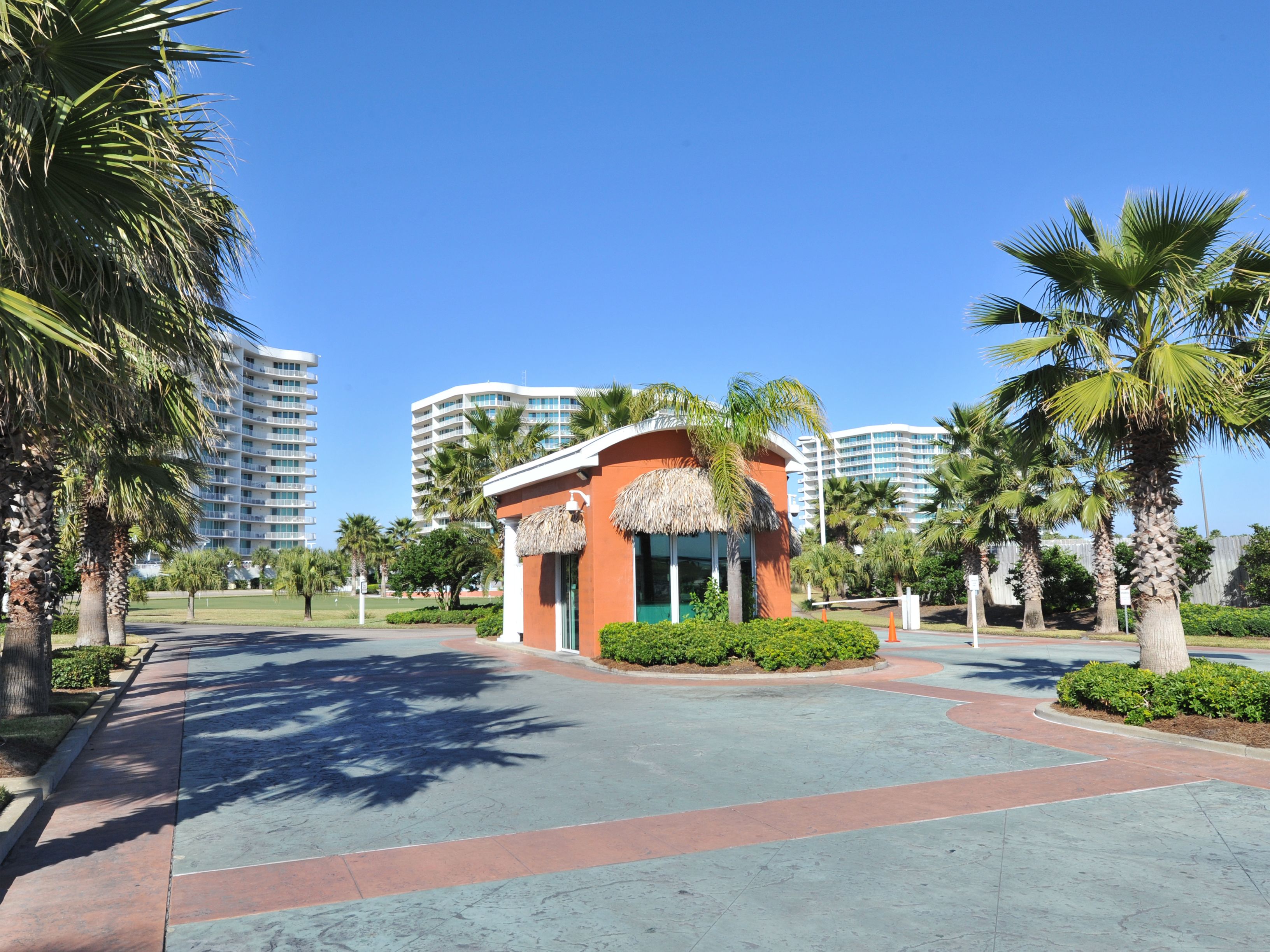 A hotel with a central building featuring a thatched roof, surrounded by palm trees and a paved walkway.