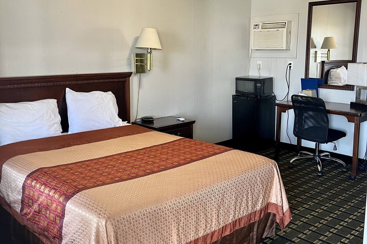 Una habitación de hotel con una cama grande, un escritorio con computadora, una silla, una lámpara y un aire acondicionado.