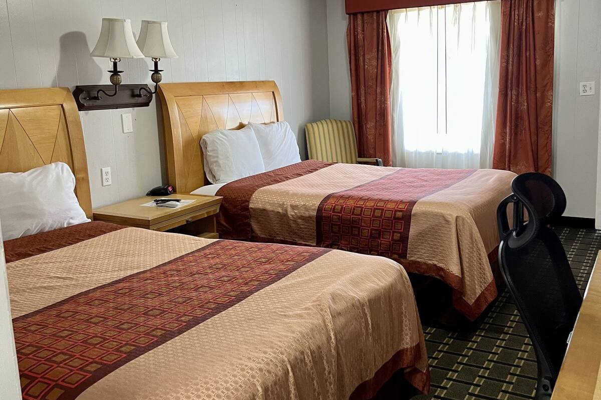 Una habitación de hotel con dos camas, un escritorio, una silla y un ventanal con cortinas.