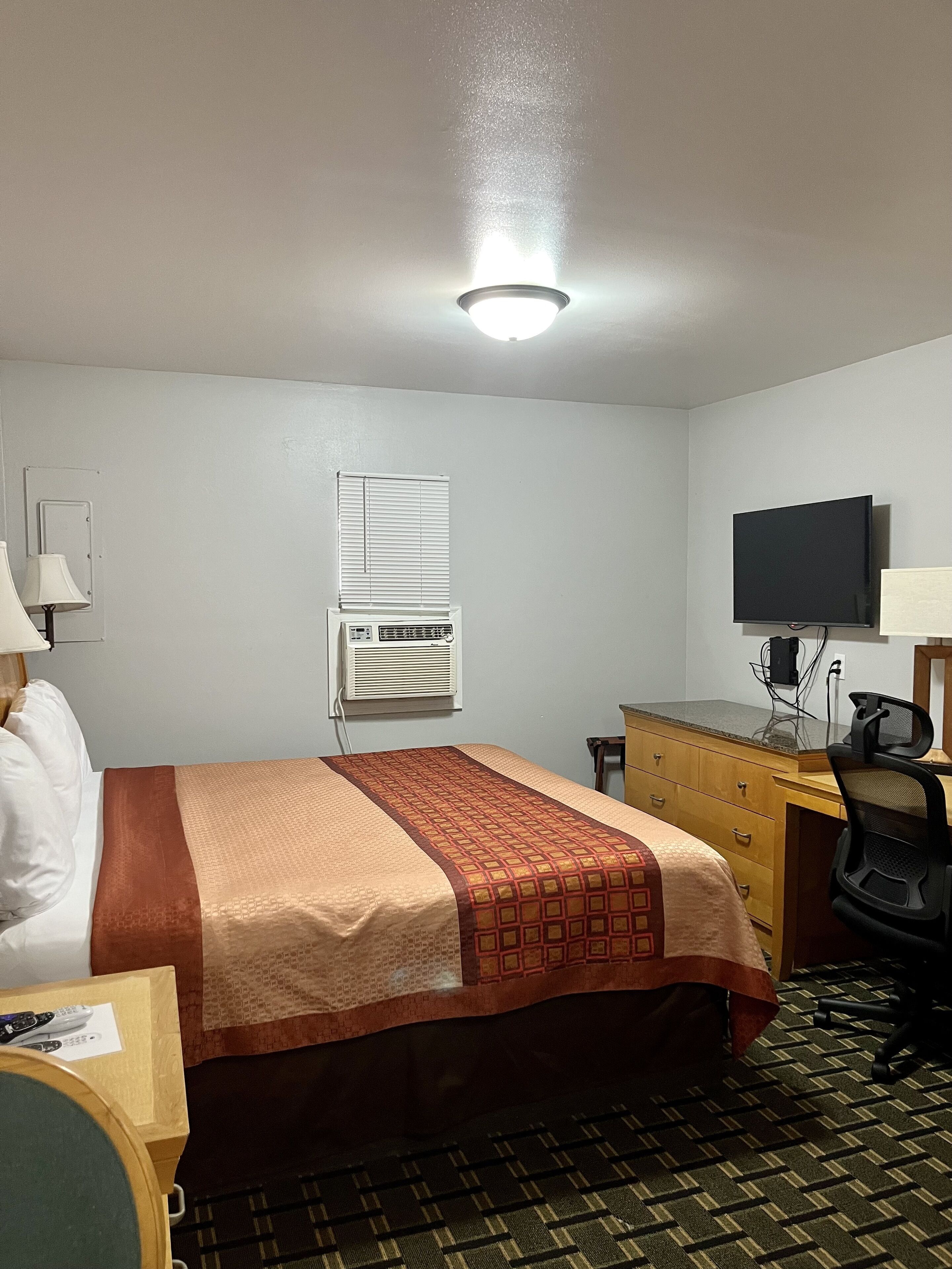 Habitación de hotel con cama, escritorio, silla, televisor, aire acondicionado y luz en el techo.