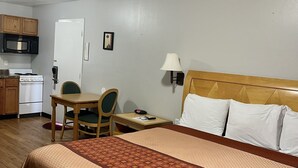 A hotel room with a bed, a desk with a chair, a microwave, a stove, and a refrigerator. - Chief Motel (Keokuk)