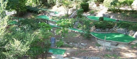 Un parcours de mini-golf doté de plusieurs zones d’entraînement au putting, entourées d’arbres et d’arbustes.
