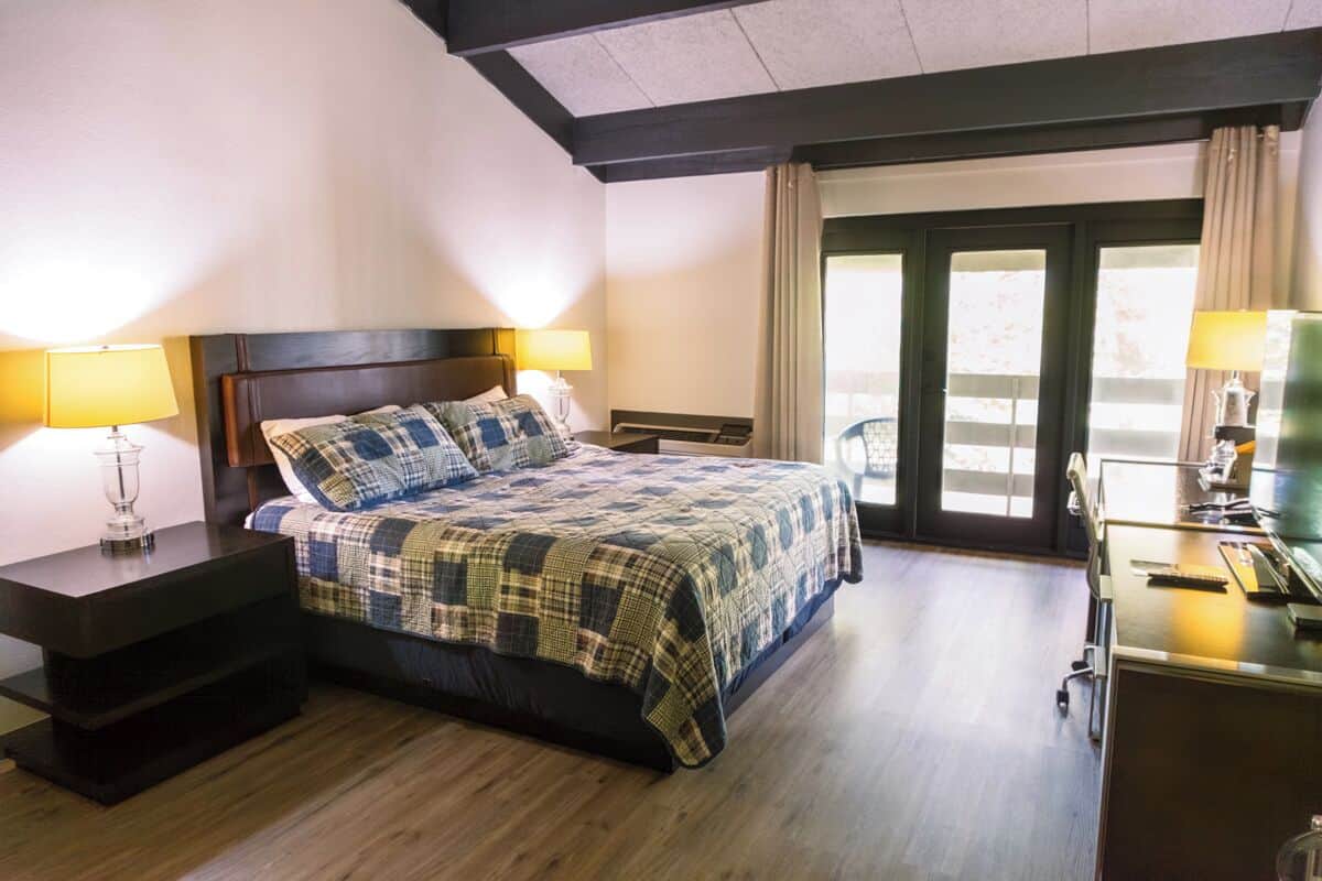 A hotel room with a bed, bedside tables, a desk, and a view through a glass door.