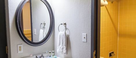 A bathroom with a vanity, mirror, towel rack, and a shower area with a bathtub.