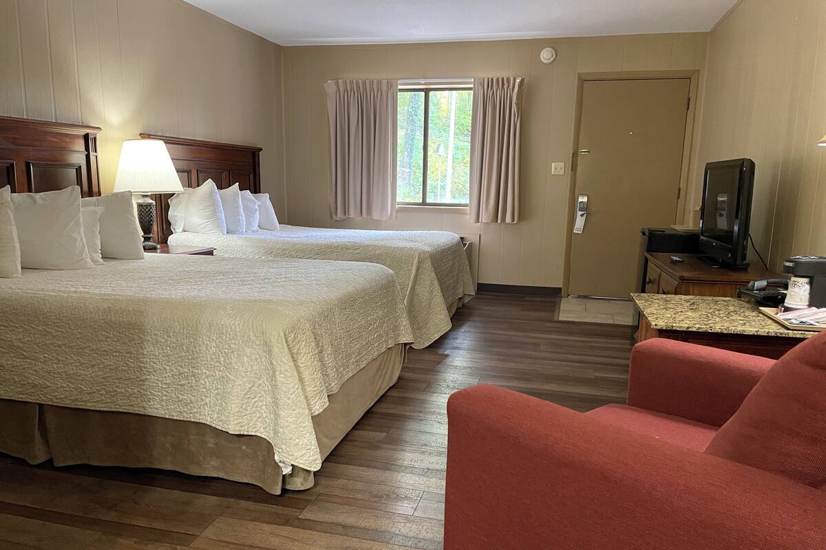 A hotel room with two beds, a television, a coffee maker, and a desk with a chair.