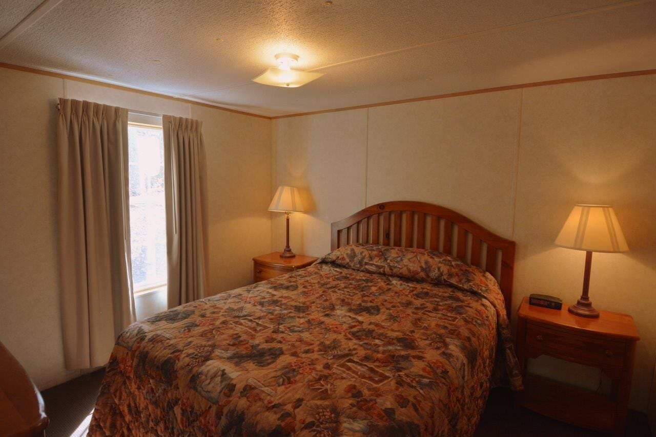 A bedroom with a bed, two bedside tables with lamps, a window with curtains, and a ceiling light.