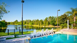 Una piscina con sillas blancas y vistas a un lago y árboles.