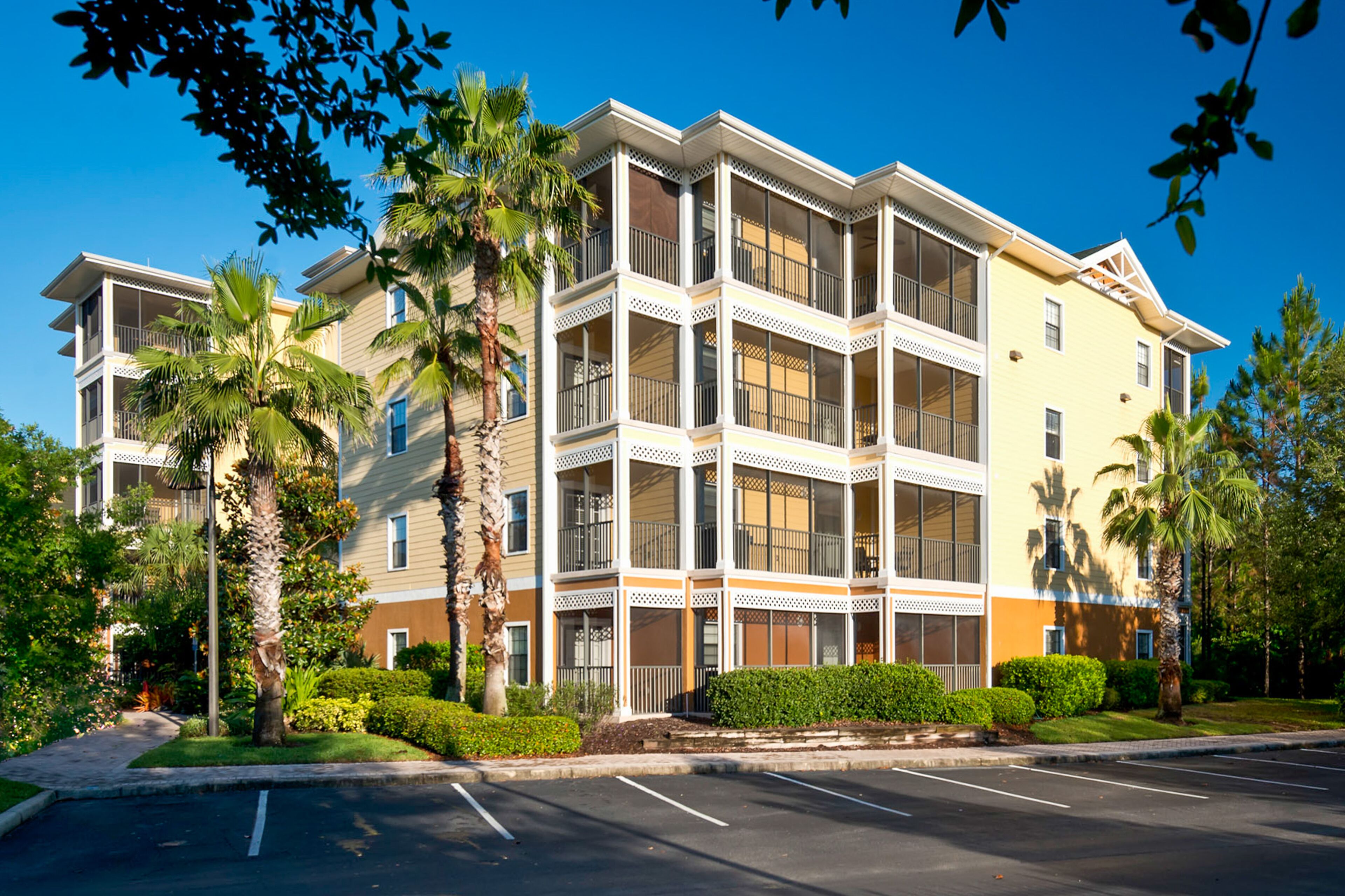 A multi-story hotel with balconies, palm trees, and a parking lot.