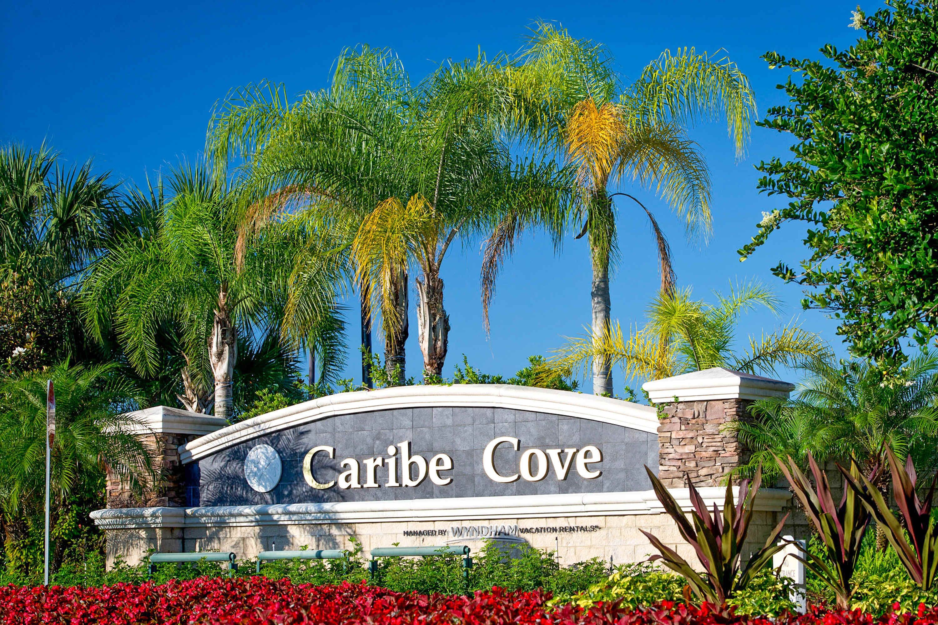 A sign for "Caribe Cove" with a stone arch and palm trees in the background.