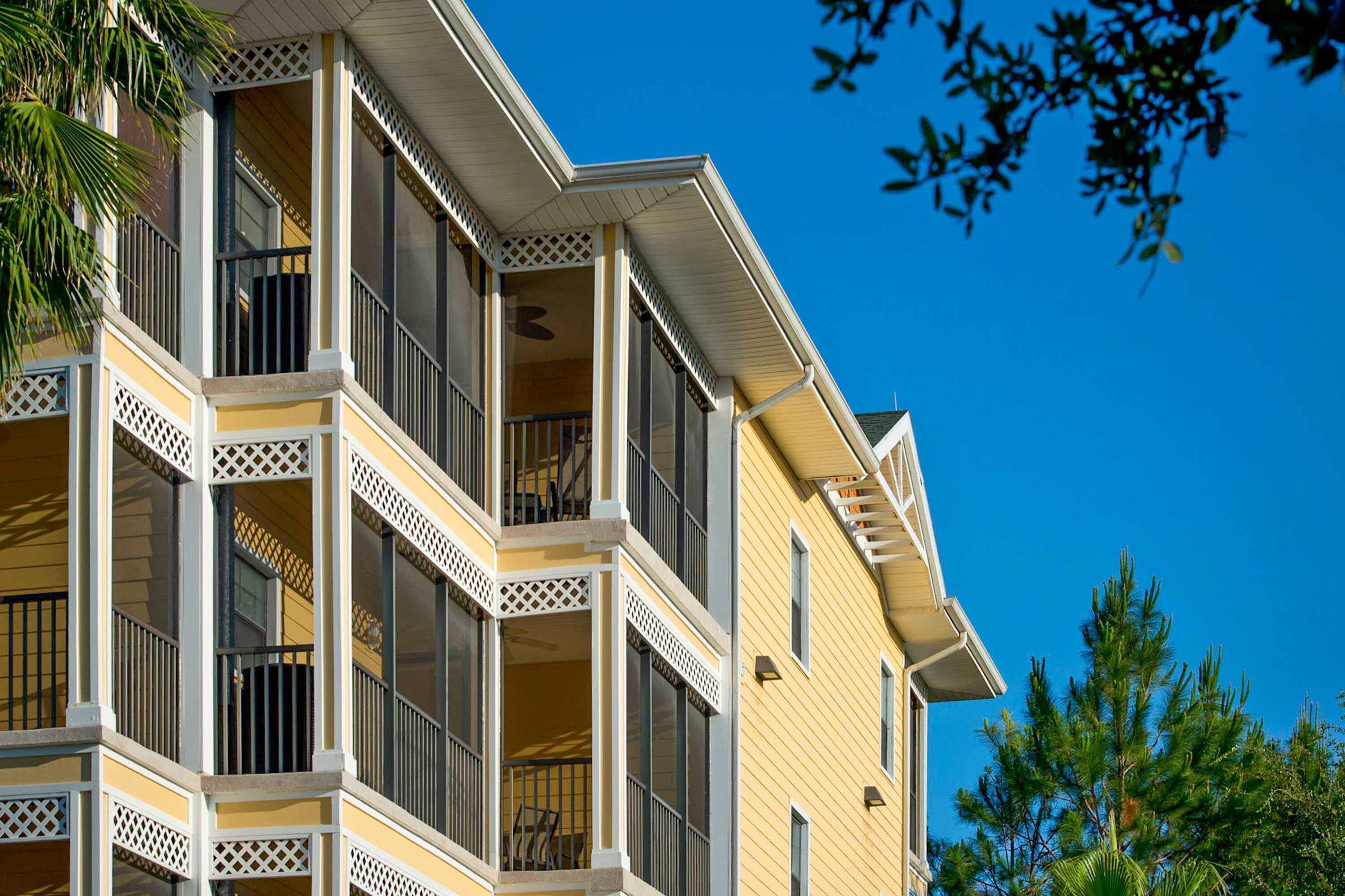 A multi-story building with balconies, a clear blue sky, and some trees.
