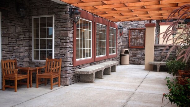 A covered patio with stone walls, wooden chairs, and a concrete floor. - TownePlace Suites by Marriott Pocatello (Pocatello)
