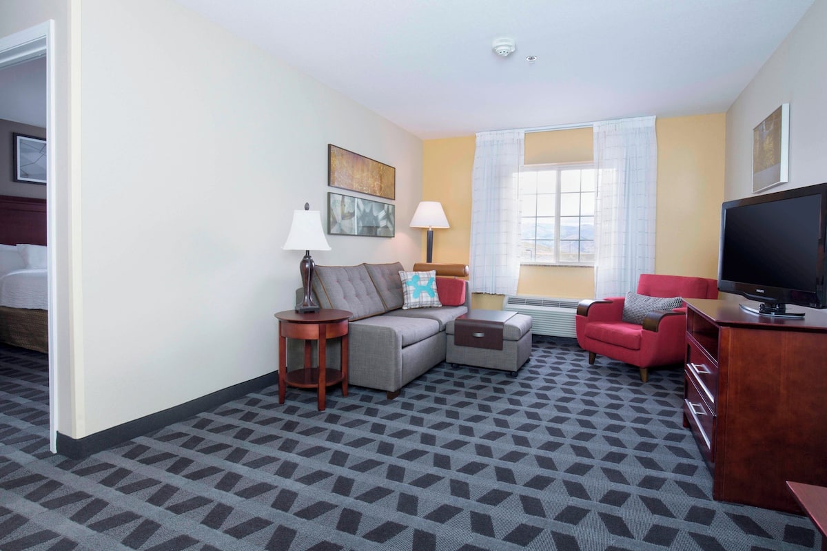 A hotel room with a sofa, a red armchair, a TV, and a desk.