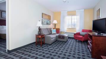 Una habitación de hotel con sofá, un sillón rojo, televisor y escritorio.