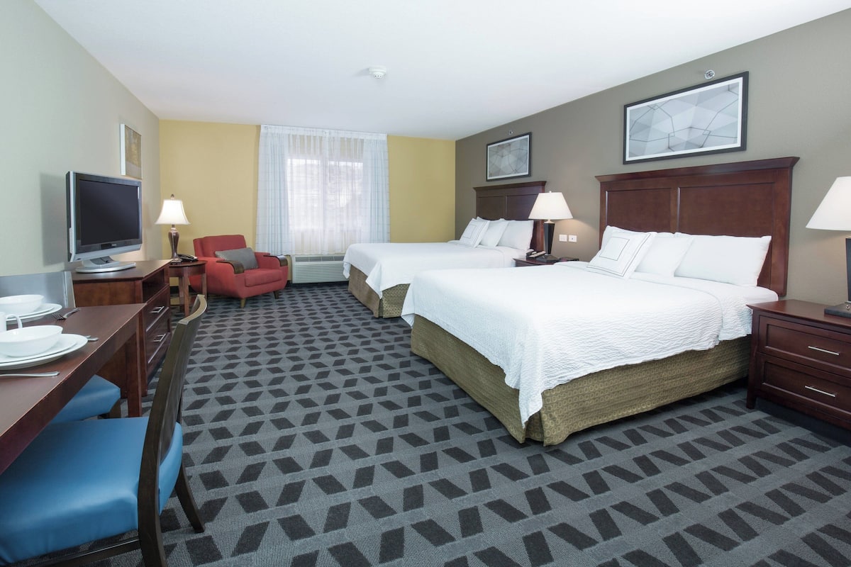 A hotel room with two beds, a desk with a TV, a chair, and a dining table.