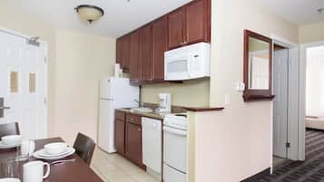 A compact kitchen with wooden cabinets, a white microwave, and a stove. There is a dining table with white plates and cups.