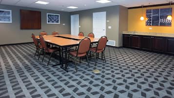 A conference room with a rectangular table, six chairs, a kitchenette, and patterned carpet.