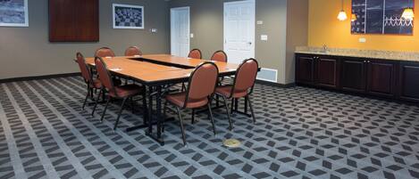 A conference room with a rectangular table, six chairs, a kitchenette, and patterned carpet.