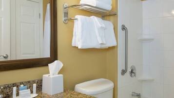 A bathroom with a toilet, a sink with toiletries, a towel rack with towels, and a shower area.