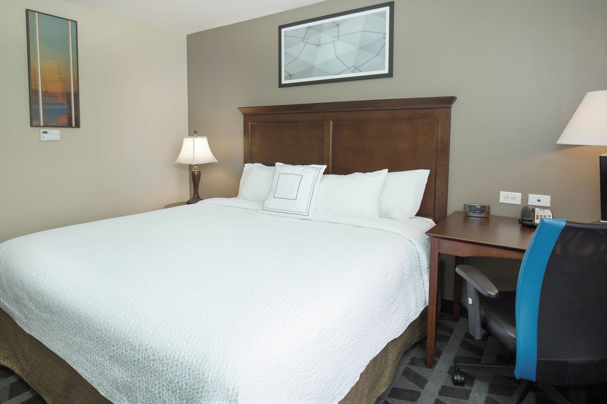 A hotel room with a large bed, a desk with a chair, a lamp, and a painting on the wall.