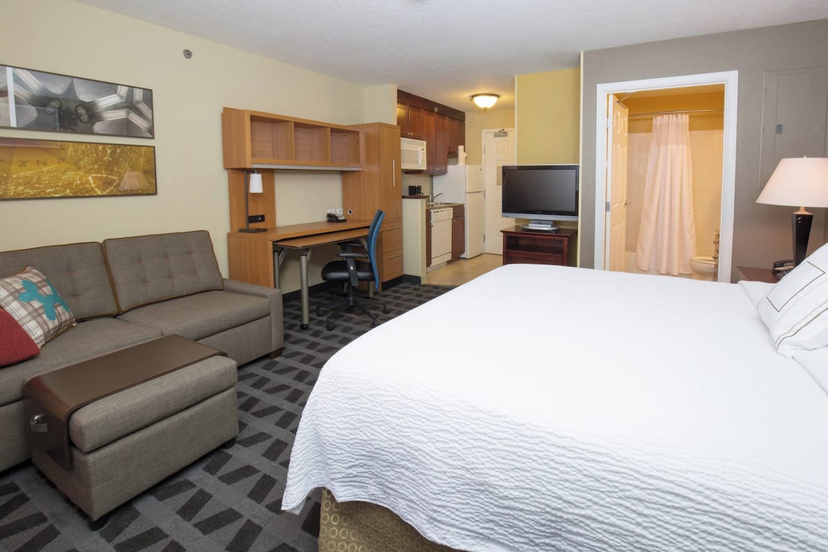 A hotel room with a bed, a sofa, a desk, a television, and a kitchenette.
