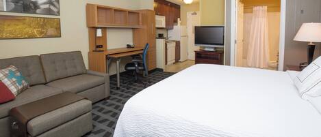 Una habitación de hotel con cama, sofá, escritorio, televisor y kitchenette.