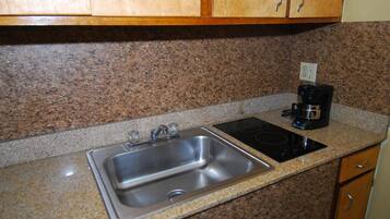 Una cocina con encimeras de granito, un lavamanos de acero inoxidable, una cafetera negra y armarios de madera.