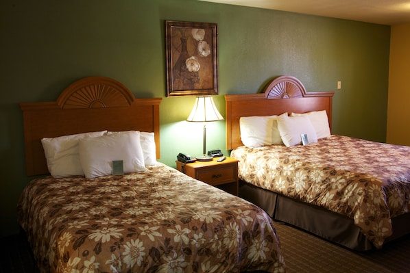 Two adjacent hotel beds with floral bedspreads, a nightstand with a lamp, and a painting on the wall.